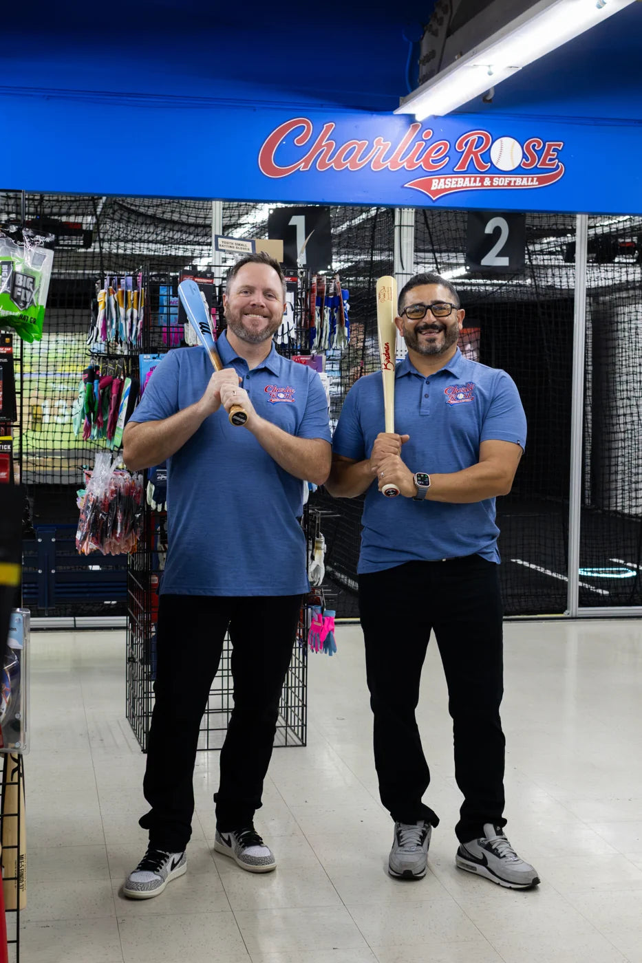 Two adults holding baseball bats inside the shop